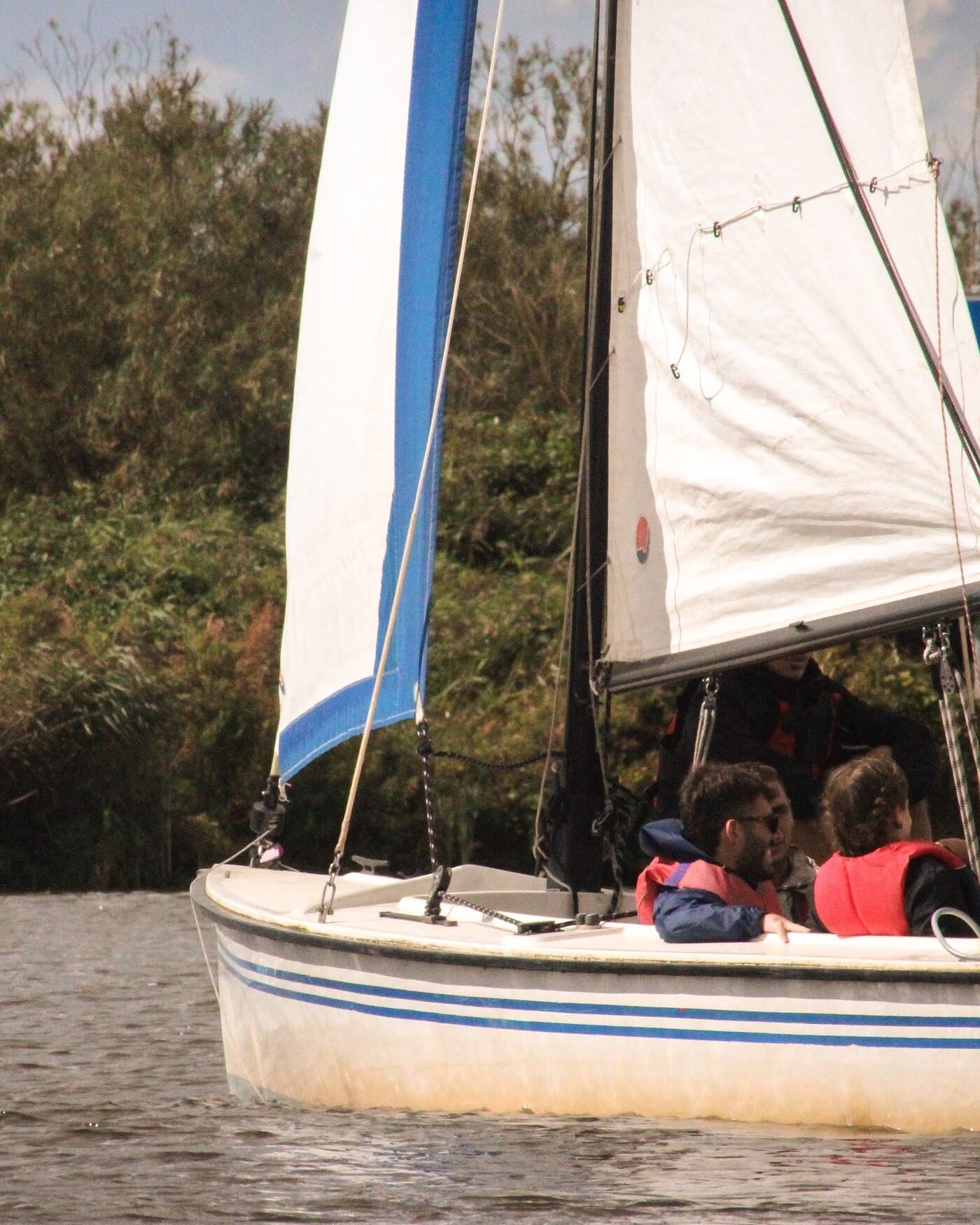 A white sailboat with a blue striped hull on a lake
